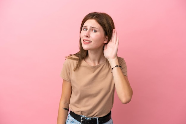 Young English woman isolated on pink background listening to something by putting hand on the ear