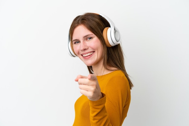 Young English woman isolated on white background listening music and pointing to the front