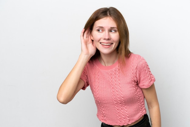 Young English woman isolated on white background listening to something by putting hand on the ear