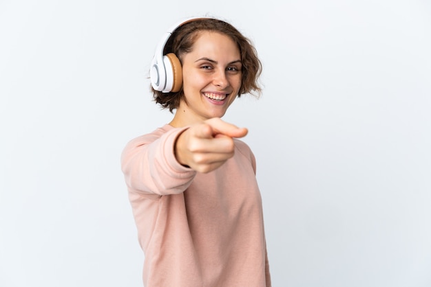 Young English woman isolated on white wall listening music and pointing to the front