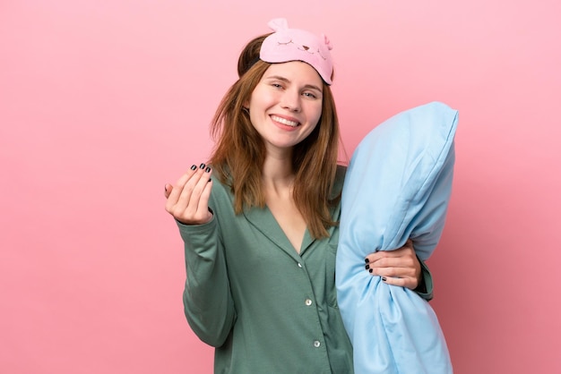 Photo young english woman in pajamas isolated on pink background in pajamas and inviting to come with hand happy that you came