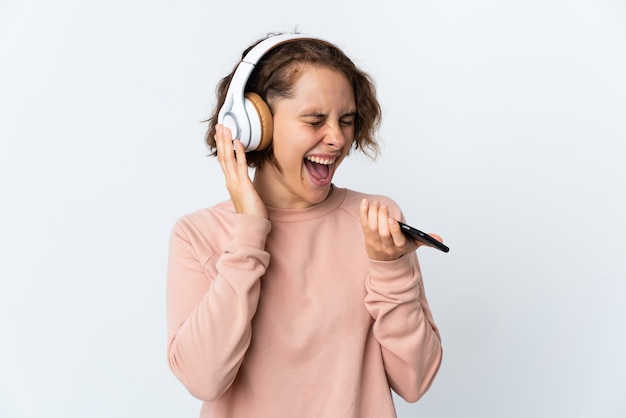 Young English woman on white listening music with a mobile and singing