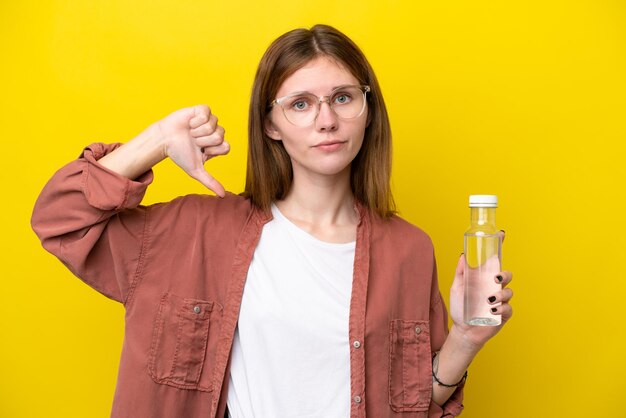 Young English woman with a bottle of water isolated on yellow background showing thumb down with negative expression