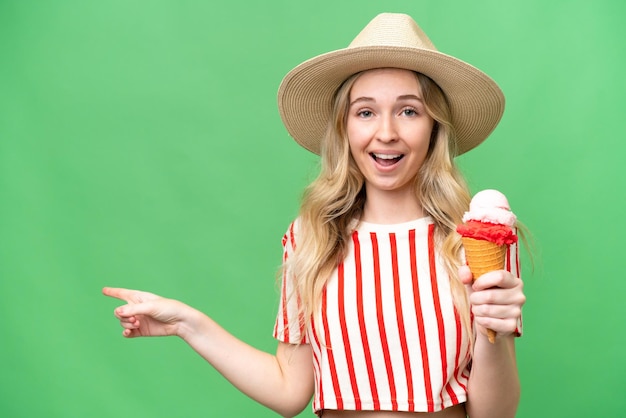 Young English woman with a cornet ice cream over isolated background surprised and pointing finger to the side