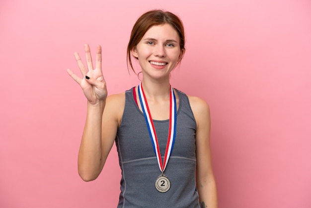 Young English woman with medals isolated on pink background happy and counting four with fingers