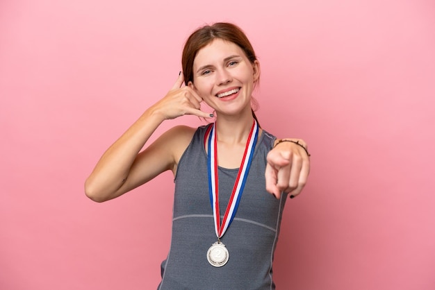 Young English woman with medals isolated on pink background making phone gesture and pointing front