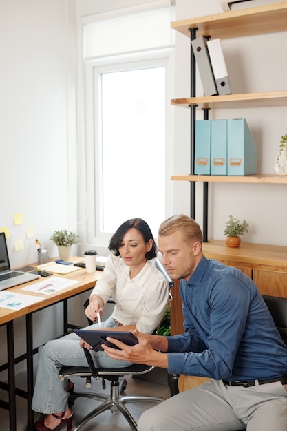 Young entrepreneur asking colleague to help him to understand chart on tablet computer