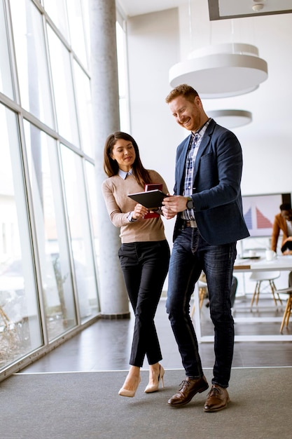 Young entrepreneur couple walking together and using digital tablet in the modern office