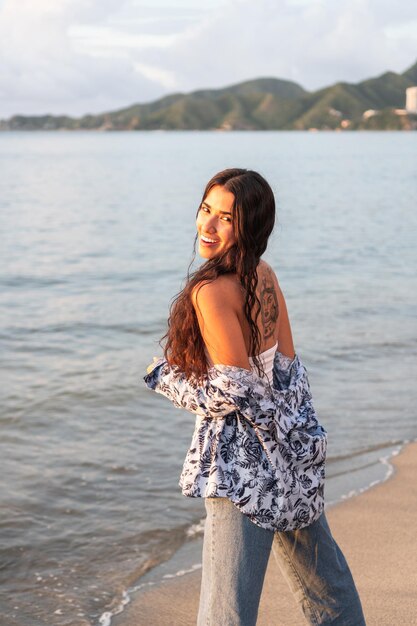 Young ethnic woman standing on the shore of the beach looking at the camera