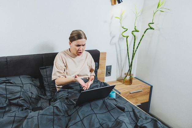 Young European beautiful woman sitting on bed with coffee working with computer at home remote work Woman happy and smiling in bed at home