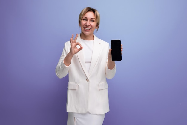 Young european blonde business woman in white jacket and dress with smartphone mockup