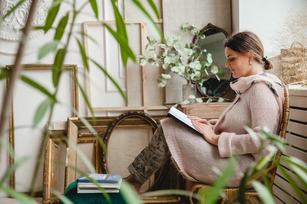 young European brunette woman in a warm beige cardigan sits in a wicker chair