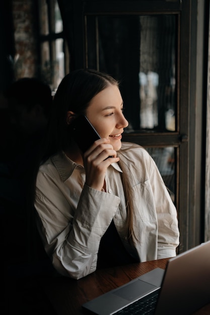 A young European freelancer girl with long dark hair drinks coffee and remotely works in a cafe