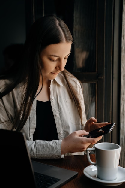 A young European freelancer girl with long dark hair remotely works and studying in a cafe