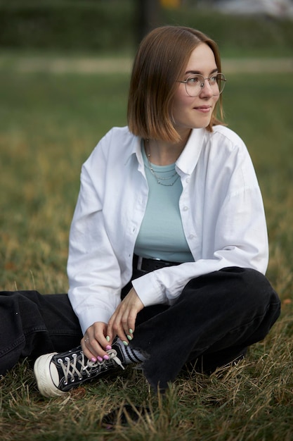 A young European girl in glasses is resting in a park on a green stave. Portrait of a girl