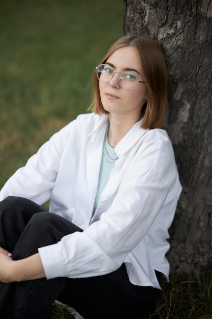 A young European girl in glasses is resting in a park on a green stave. Portrait of a girl