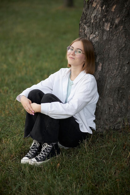 A young European girl in glasses is resting in a park on a green stave. Portrait of a girl