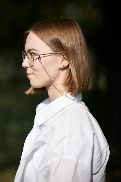 A young European girl in glasses is resting in a park on a green stave. Portrait of a girl