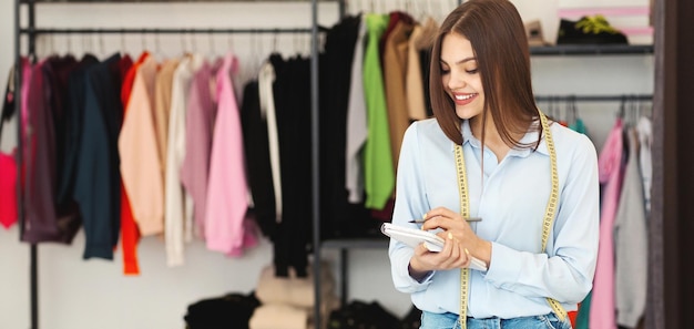 Photo young european woman boutique owner smiling while taking notes with colorful clothing in the