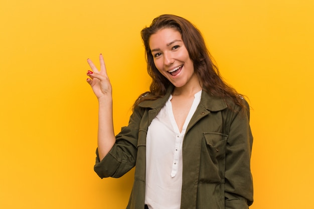 Young european woman isolated over yellow  joyful and carefree showing a peace symbol with fingers.