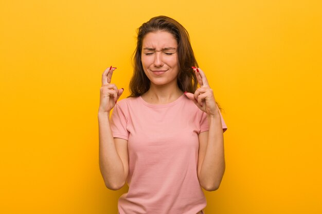 Young european woman isolated over yellow wall crossing fingers for having luck