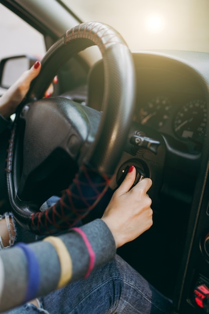 A young European woman with healthy clean skin put her hands with red manicure on her nails on the steering wheel of the car and the ignition key. Traveling and driving concept.