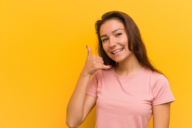 Young european woman over yellow wall showing a mobile phone call gesture with fingers.