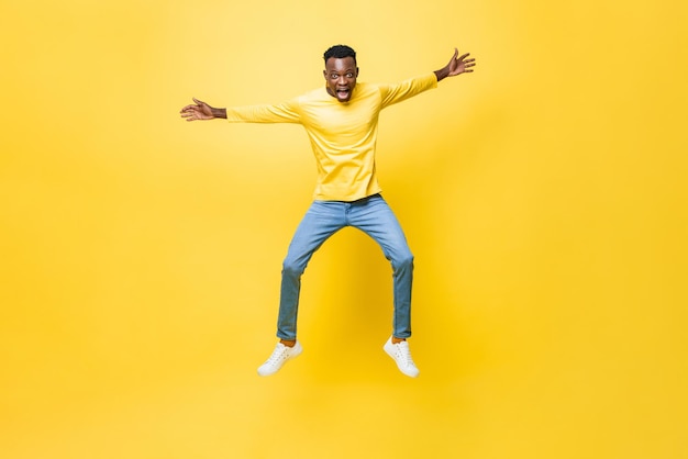 Young excited African man jumping with outstretched hands isolated on yellow studio background