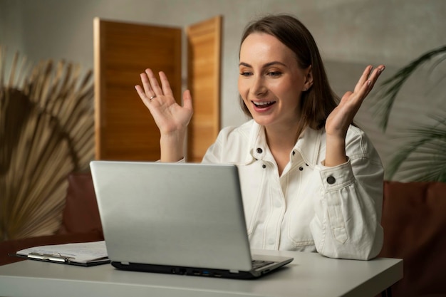 Young excited happy brunette woman in a white shirt who has achieved success using a laptop winning