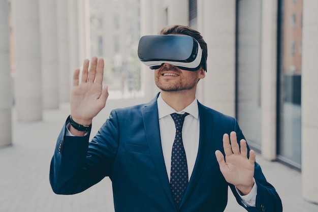 Young excited man in suit standing on city street and testing VR glasses or 3d goggles