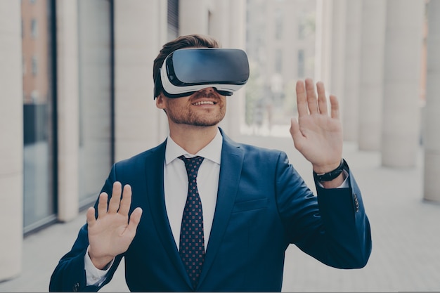 Young excited man in suit standing on city street and testing vr glasses or d goggles