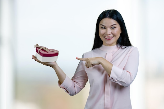 Young expressive asian woman showing heartshaped gift box