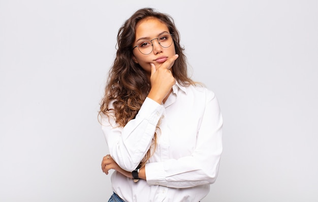 young expressive woman with glasses and elegant white blouse posing on white wall