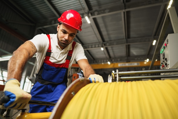 A young factory workman rolls heavy coil of electric cable