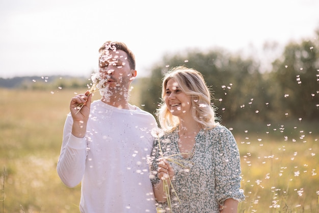 Young family blowing dandelions on each other and laughing, man and woman