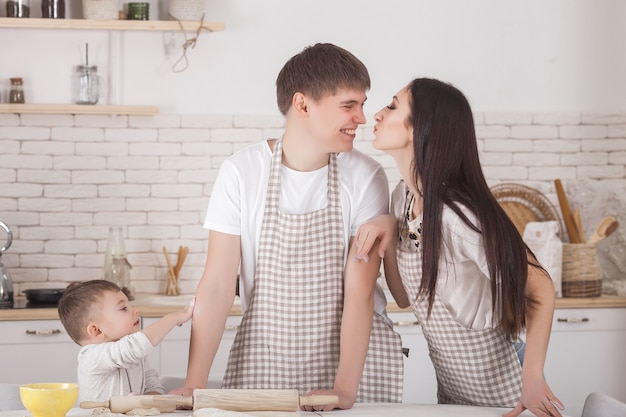 Young family cooking together. Husband, wife and their little baby on the kitchen. Family 
kneading the dough with flour. People cook the dinner or breakfast.