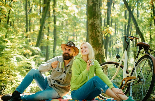 Photo young family couple have picnic in autumnal park man and woman sitting on picnic blanket and drinking hot coffee bicycle ride and active lifestyle romantic picnic concept