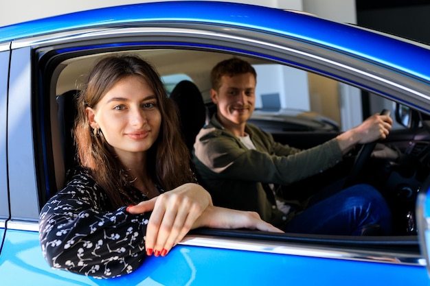 A young family is sitting in a new car at a dealership A young woman looks at the camera