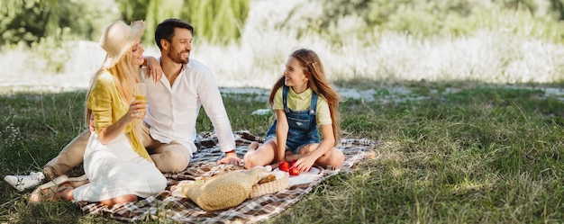 Young family picnicking with their cute daughter sitting on blanket in park