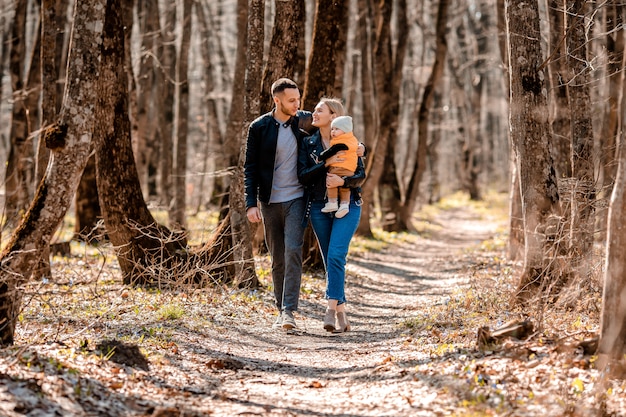 Young family walk in the park in the spring with a toddler in a stroller. Happy parents