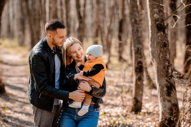 Young family walk in the park in the spring with a toddler in a stroller. Happy parents