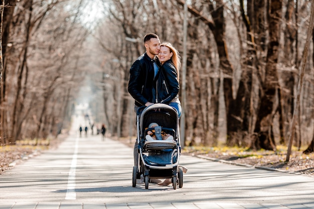 Young family walk in the park in the spring with a toddler in a stroller. Happy parents