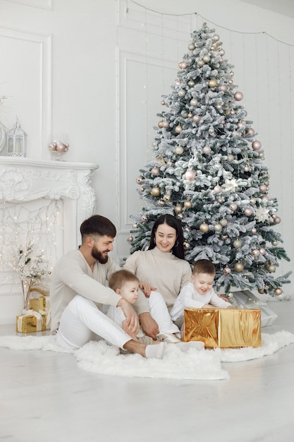 Young family in white clothes sitting near Christmas tree