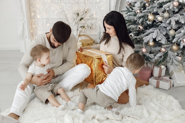 Young family in white clothes sitting near Christmas tree