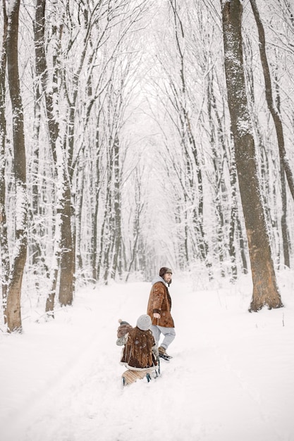 Young family with baby boy riding on a sled in winter forest