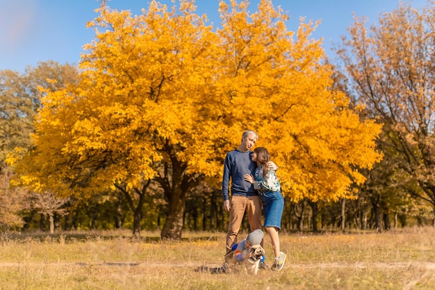 A young family with a small child and a dog spend time together for a walk in the autumn park