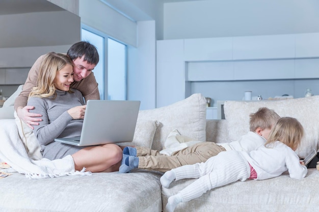 A young family with small children sit on a white sofa in a modern living room with gadgets Love tenderness and harmony in relationships