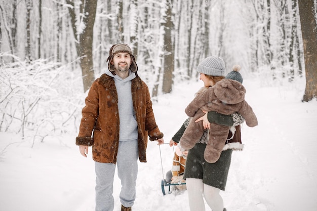 Young family with two children riding on a sled in winter forest