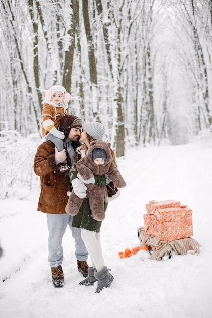 Young family with two children standing in winter forest and posing for a photo