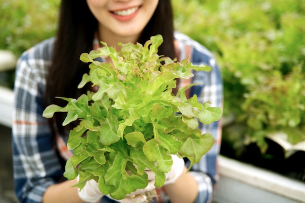 Young farmer girl holding red oak lettuce in hydroponic farm with smile